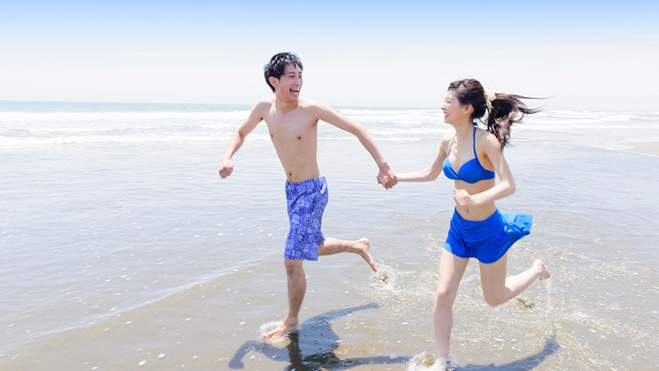 ビーチで男女が笑いながら走っている写真