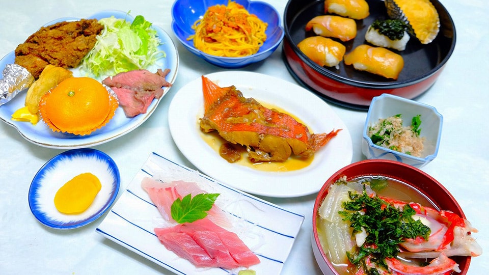 民宿椿荘の夕食の一例（刺身、魚の煮付け、寿司がならぶ様子）