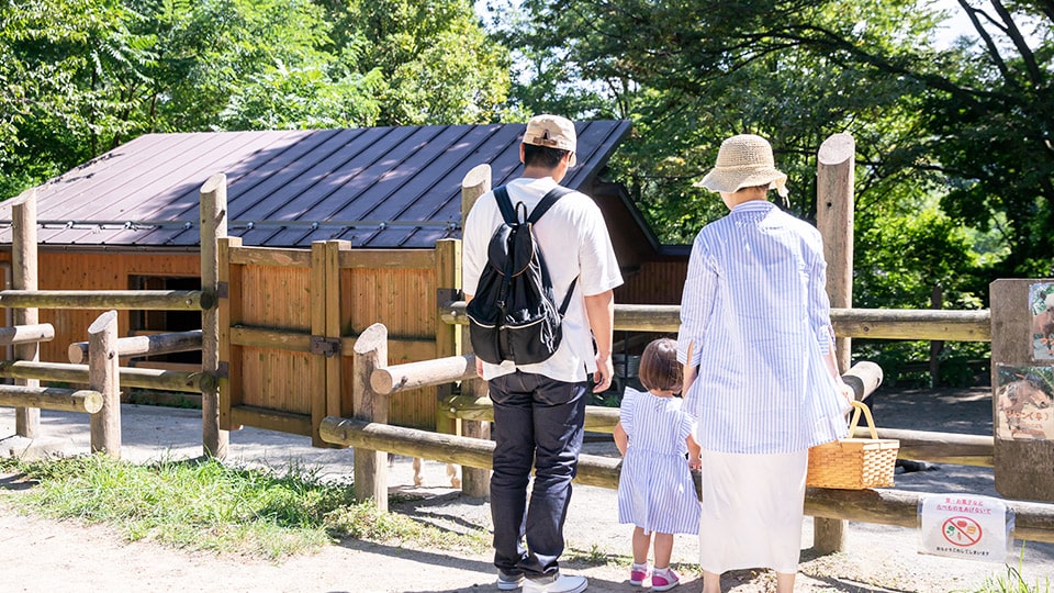 動物園またはふれあい牧場で、木製の柵と小屋の前に立つ親子連れ